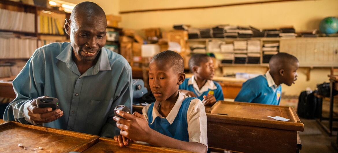 Partially blind teacher Samuel Atuhairwe assists student Patricia Karungi with operating a Victor reader in a classroom at St. Bernadette Primary school in Uganda.