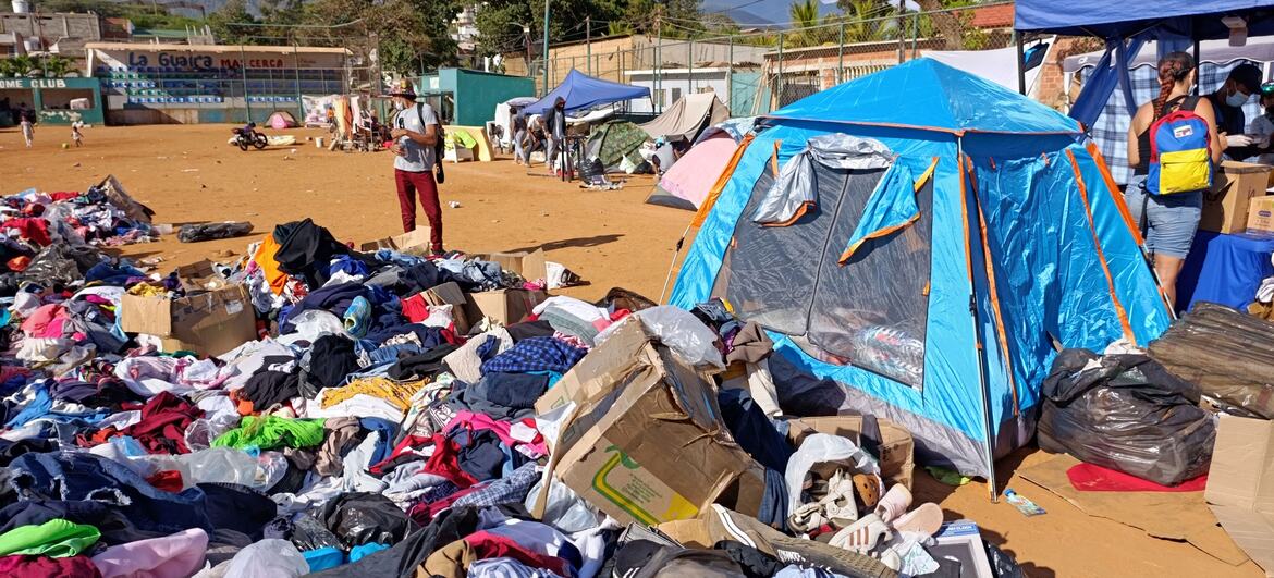 A temporary shelter with blue tents and piles of donated clothing for people displaced by the 2026 earthquakes in La Guaira, Venezuela.