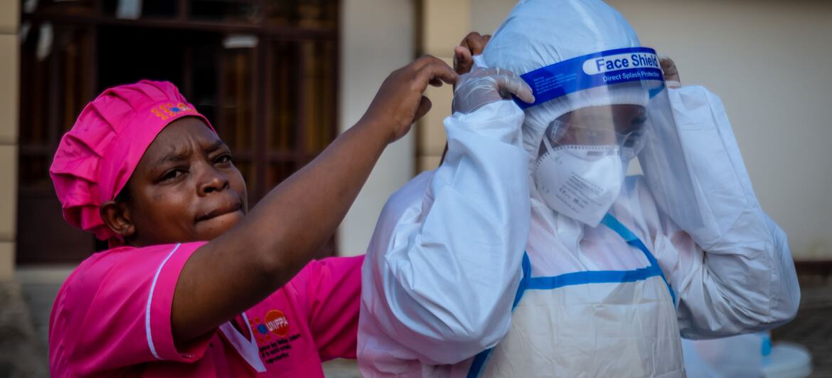 A midwife in a pink uniform helps a colleague adjust a face shield during a PPE practical session in North Kivu.