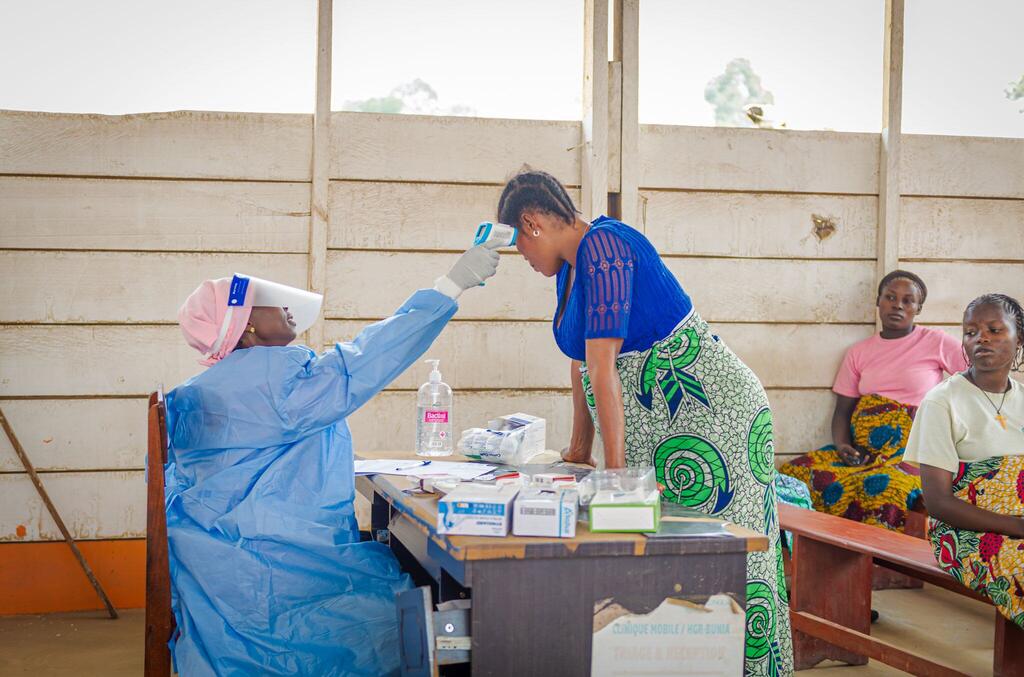 Une sage-femme vêtue d'une combinaison de protection bleue prend la température d'une femme enceinte dans un centre de santé d'un camp de déplacés en République démocratique du Congo, en pleine épidémie d'Ebola.