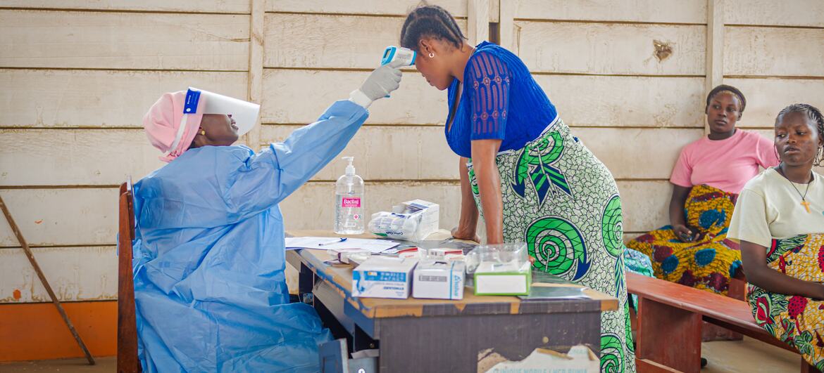 Una comadrona con traje protector azul le toma la temperatura a una mujer embarazada en un centro de salud en un campamento de desplazados en la República Democrática del Congo durante un brote de ébola.
