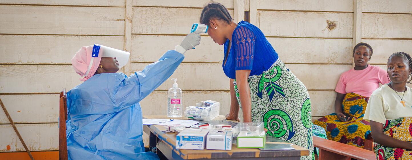 Une sage-femme vêtue d'une combinaison de protection bleue prend la température d'une femme enceinte dans un centre de santé d'un camp de déplacés en République démocratique du Congo, en pleine épidémie d'Ebola.