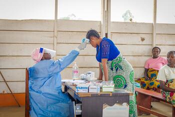 Une sage-femme vêtue d'une combinaison de protection bleue prend la température d'une femme enceinte dans un centre de santé d'un camp de déplacés en République démocratique du Congo, en pleine épidémie d'Ebola.