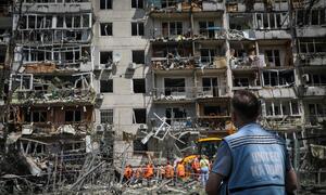 Au premier plan, un homme portant un gilet des Nations Unies observe un immeuble d'habitation fortement endommagé à Kyiv, en Ukraine, où des équipes de recherche et de sauvetage travaillent parmi les décombres.