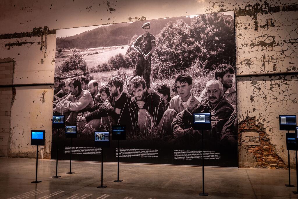 Une grande photographie historique est exposée au mémorial de Srebrenica, montrant des survivants et des victimes du massacre de 1995. L'exposition comprend des panneaux d'information et des écrans vidéo.
