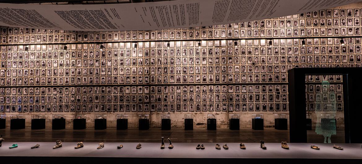 An interior view of the Srebrenica Genocide Memorial, featuring a wall of victims' portraits and a display of shoes belonging to the men and boys who were killed.