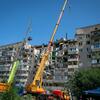 Heavy machinery, including large cranes and a dump truck, are at the scene of a damaged multi-story residential building in Kyiv, Ukraine.