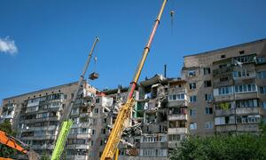 Des engins lourds, dont de grandes grues et un camion-benne, sont sur les lieux d'un immeuble résidentiel de plusieurs étages endommagé à Kyiv, en Ukraine.