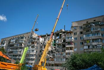 Des engins lourds, dont de grandes grues et un camion-benne, sont sur les lieux d'un immeuble résidentiel de plusieurs étages endommagé à Kyiv, en Ukraine.