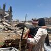 امرأة فلسطينية تحمل طفلاً صغيراً بينما تنظر إلى الأنقاض في غزة.