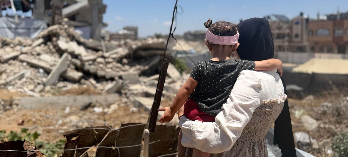 امرأة فلسطينية تحمل طفلاً صغيراً بينما تنظر إلى الأنقاض في غزة.