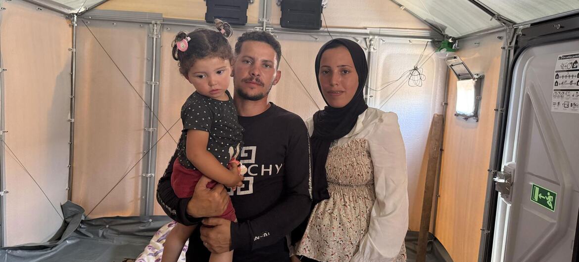 A Palestinian family, including a pregnant woman named Mayyada and her daughter Mila, stands inside a temporary shelter tent in Gaza.