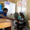 Un responsable de l'OIM remet un kit à une mère tenant son bébé dans un bureau en Haïti.