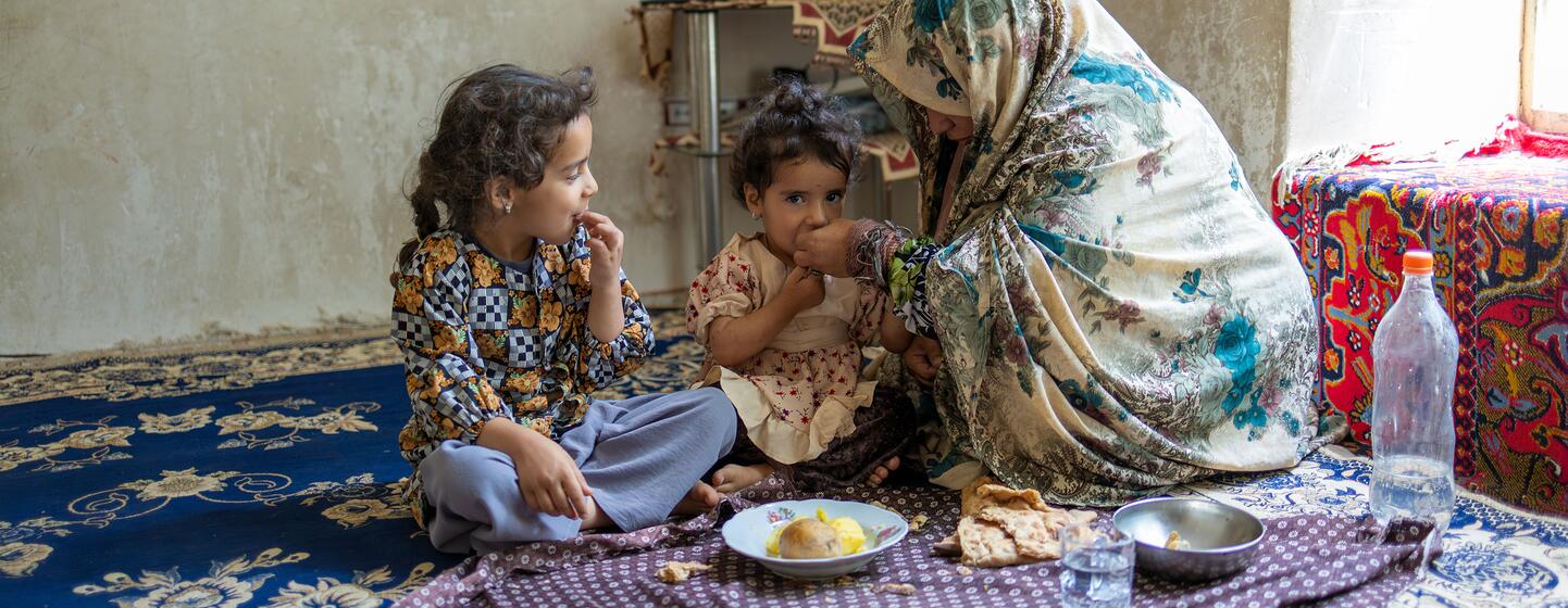 Une mère afghane partage un repas avec ses deux jeunes filles à l'intérieur de leur maison.