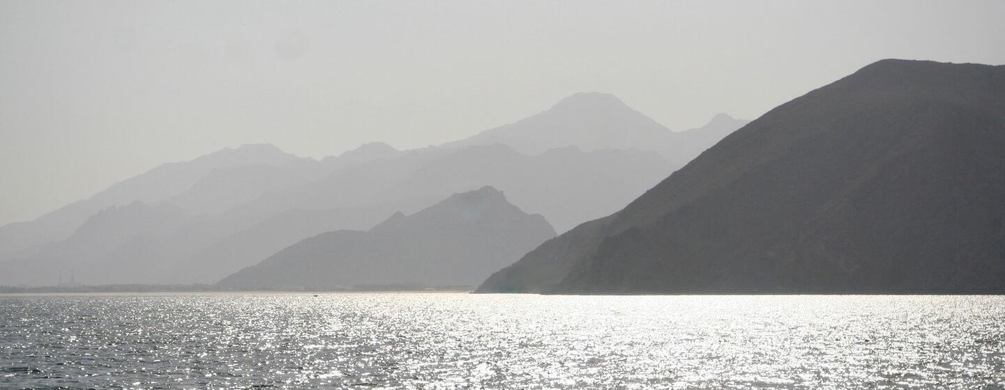 Une vue ensoleillée de la mer d'Arabie, avec un littoral brumeux et des montagnes lointaines en arrière-plan.