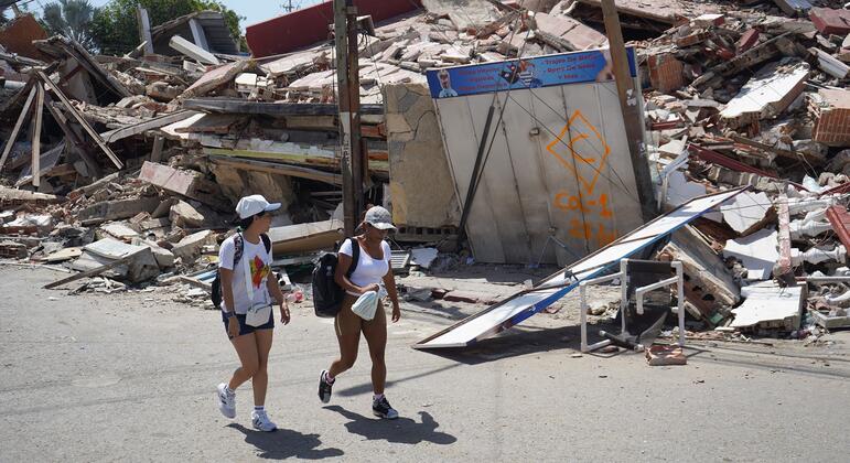 Dos jóvenes caminan por una calle pública junto a un edificio derrumbado en Catia La Mar, La Guaira, Venezuela, tras un terremoto.