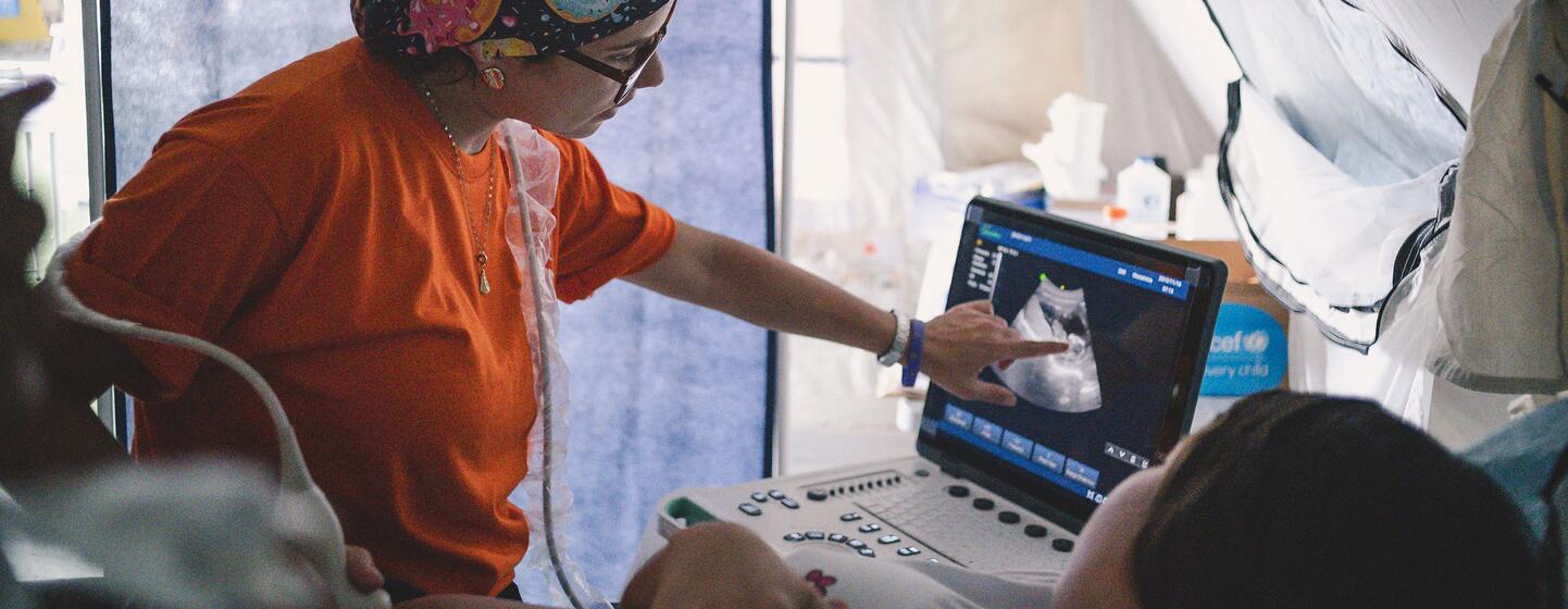 A medical professional performs an ultrasound on a patient inside a temporary tent structure.