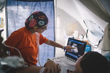 A medical professional performs an ultrasound on a patient inside a temporary tent structure.