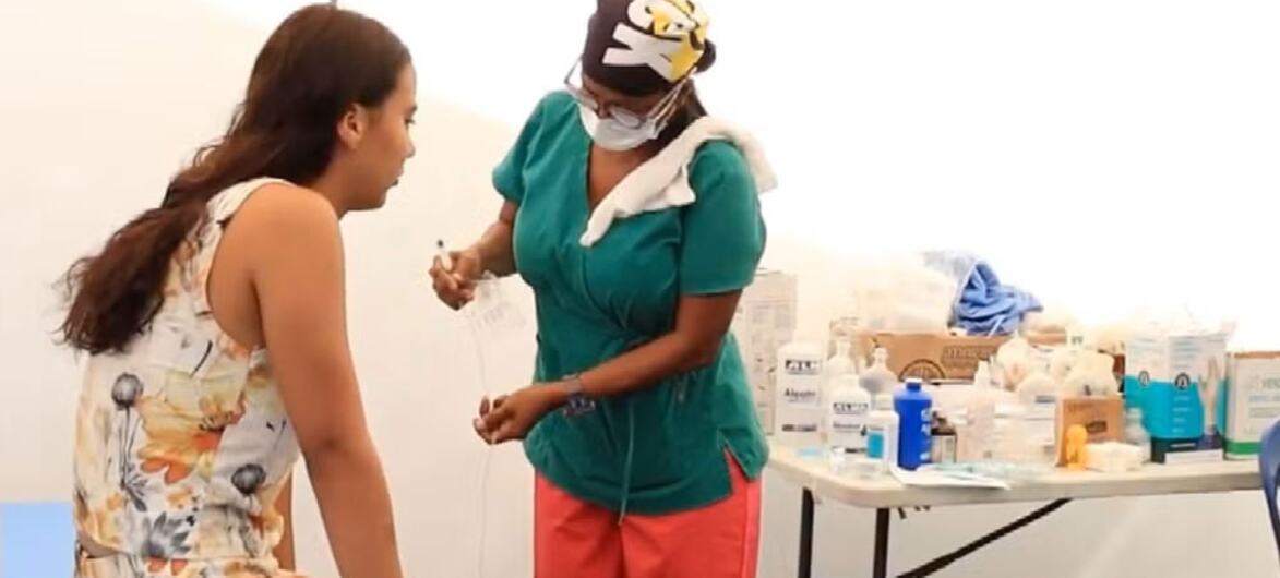 A healthcare worker in green scrubs and a face mask provides care to a pregnant woman in a medical tent in Venezuela.