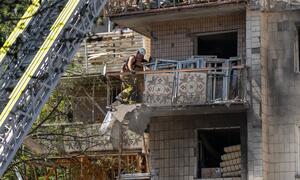 Mzima moto aliyevaa vifaa vya kujikinga amesimama kwenye balcony iliyoharibika ya jengo lililoharibiwa huko Kyiv, Ukraine, huku lori la ngazi likiwa karibu.