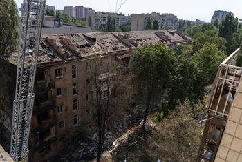 Damaged residential building in Kyiv, Ukraine, with a destroyed roof and rubble in the foreground.