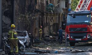 Bombeiros e um caminhão de bombeiros no local de um ataque em Kiev, na Ucrânia, cercados por um prédio danificado e escombros.