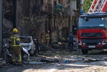 Firefighters and a fire truck at the scene of an attack in Kyiv, Ukraine, surrounded by a damaged building and debris.