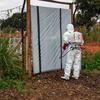 Mfanyakazi wa afya aliyevalia suti nyeupe ya hatari akisafisha mlango wa kuingia kwenye chumba cha kuhifadhia maiti katika kituo cha matibabu ya Ebola katika Jamhuri ya Kidemokrasia ya Kongo.
