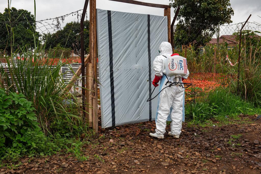 Un agent de santé vêtu d'une combinaison de protection blanche désinfecte l'entrée d'une morgue dans un centre de traitement d'Ebola en République démocratique du Congo.