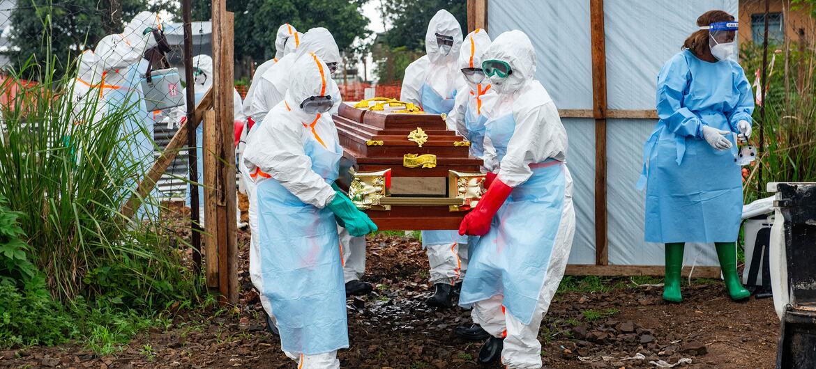 Members of a community-based Safe and Dignified Burial team in protective gear prepare to carry a casket at the Rwampara Ebola Treatment Centre in the Democratic Republic of the Congo.