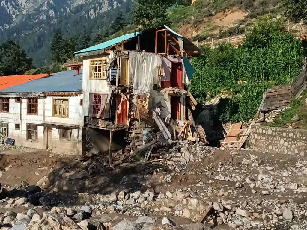 Une maison partiellement effondrée dans un village de montagne, entourée de rochers et de débris suite à une crue éclair.