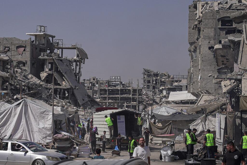 Des employés du PAM , vêtus de gilets verts, distribuent des repas chauds aux familles de Jabalyiah, à Gaza, au milieu des décombres des bâtiments détruits.