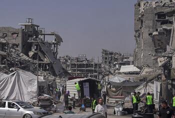 WFP workers in green vests distribute hot meals to families in Jabalyiah, Gaza, amidst the rubble of destroyed buildings.