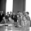 Autoridades no Palácio das Nações, em Genebra, assinam a Convenção Relativa ao Estatuto dos Refugiados em 1951. Sentados à mesa estão, da esquerda para a direita, Margaret Kitchen, John Humphrey, Knud Larsen e o Dr. G.J. Van Heuven Goedhart, com outros delegados e observadores em pé atrás deles.