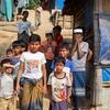 Un groupe d'enfants dans un camp de réfugiés rohingyas au Bangladesh, debout sur un chemin bordé de sacs de sable près d'un abri en bambou.