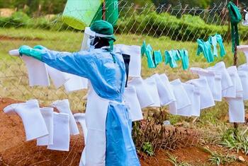 Health worker in protective gear hangs white bags on a fence during an Ebola response operation in the Democratic Republic of Congo.