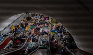 A crowded Kyiv metro station in Ukraine, filled with families sheltering from overnight air-raid attacks. People, including children, are seen sleeping and resting on the floor and on escalators.