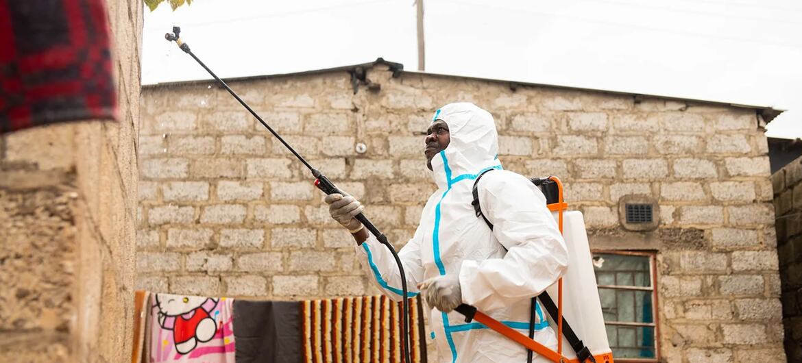 Um voluntário com um traje de proteção branco desinfeta a fachada de um prédio com um pulverizador.