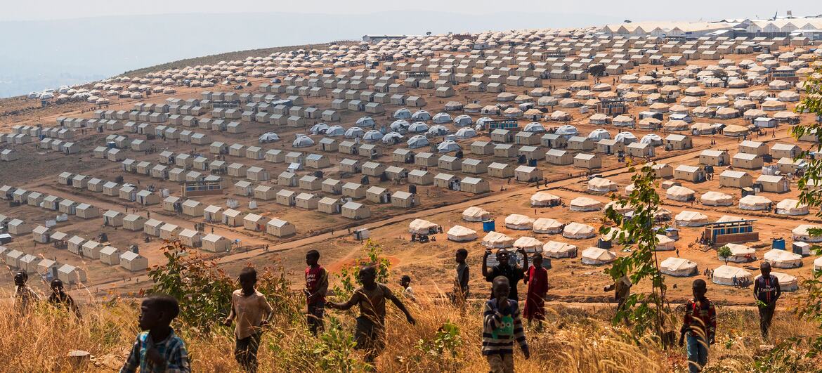 A wide view of a large refugee camp on a hillside in Burundi, with rows of tents and children in the foreground.
