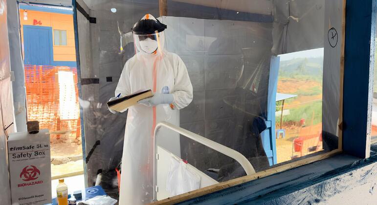 Un agent de santé en tenue de protection complète se tient à l'intérieur d'un centre de traitement d'Ebola à Nizi, en RDC, en train d'examiner un dossier médical.