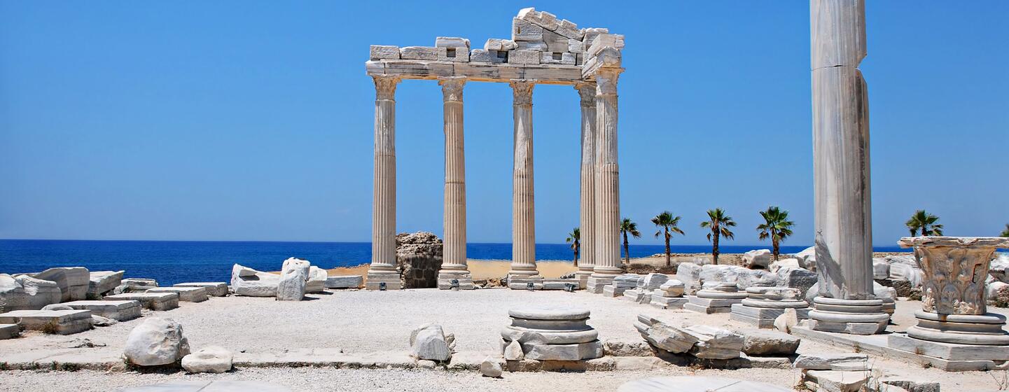 The Temple of Apollo in Side, Türkiye, with its restored Corinthian columns and stone ruins overlooking the Mediterranean Sea under a clear blue sky.