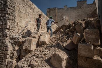 Two men clear large stones and rubble from a destroyed site in Syria.