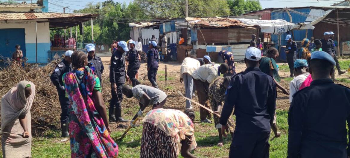 UNMISS police officers in blue helmets and uniforms stand among civilians working in a rural settlement in Kodok, South Sudan.