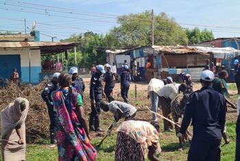 UNMISS police officers in blue helmets and uniforms stand among civilians working in a rural settlement in Kodok, South Sudan.