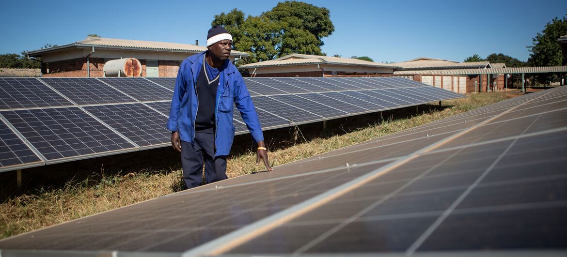 A man in a blue jacket and beanie inspects rows of solar panels installed outside Nkayi District Hospital in Bulawayo, Zimbabwe.
