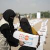 Au Yémen, une femme vêtue d'un gilet beige et d'un niqab noir remet une boîte d'aide humanitaire à une autre femme.