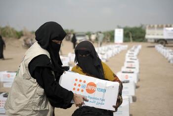 Au Yémen, une femme vêtue d'un gilet beige et d'un niqab noir remet une boîte d'aide humanitaire à une autre femme.