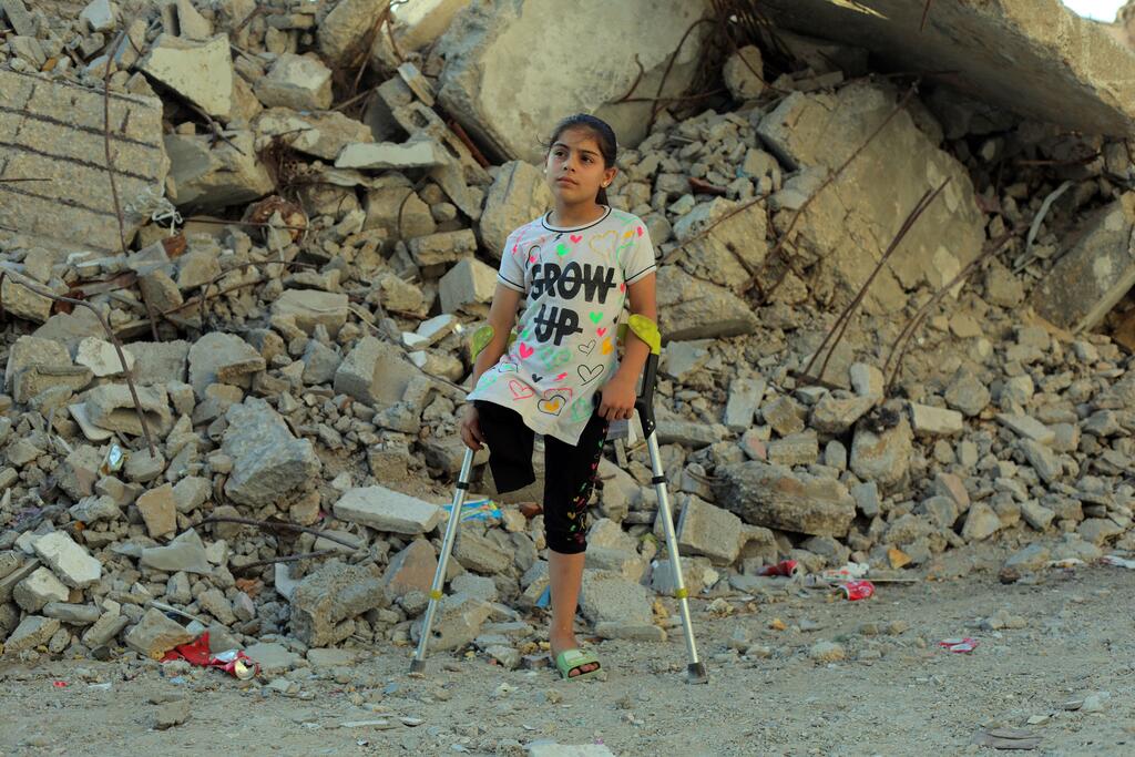 Meral, neuf ans, se tient debout sur des béquilles devant des décombres à Nuseirat, dans la bande de Gaza.