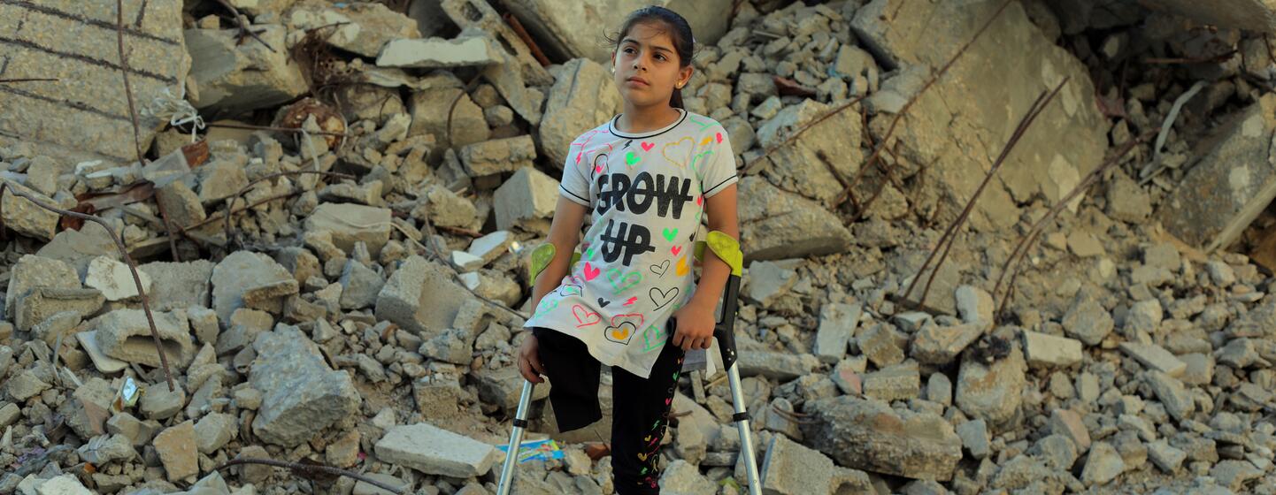 Meral, neuf ans, se tient debout sur des béquilles devant des décombres à Nuseirat, dans la bande de Gaza.