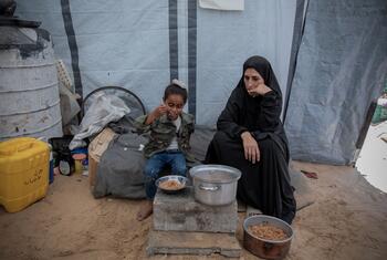 A Palestinian woman and a young girl eat food aid from bowls inside a makeshift shelter in a camp in Gaza.